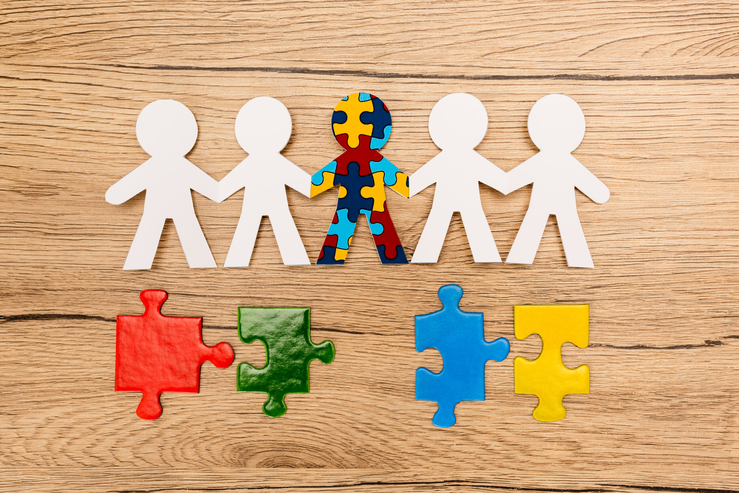Top view of special kid with autism among another with colorful pieces of puzzle on wooden